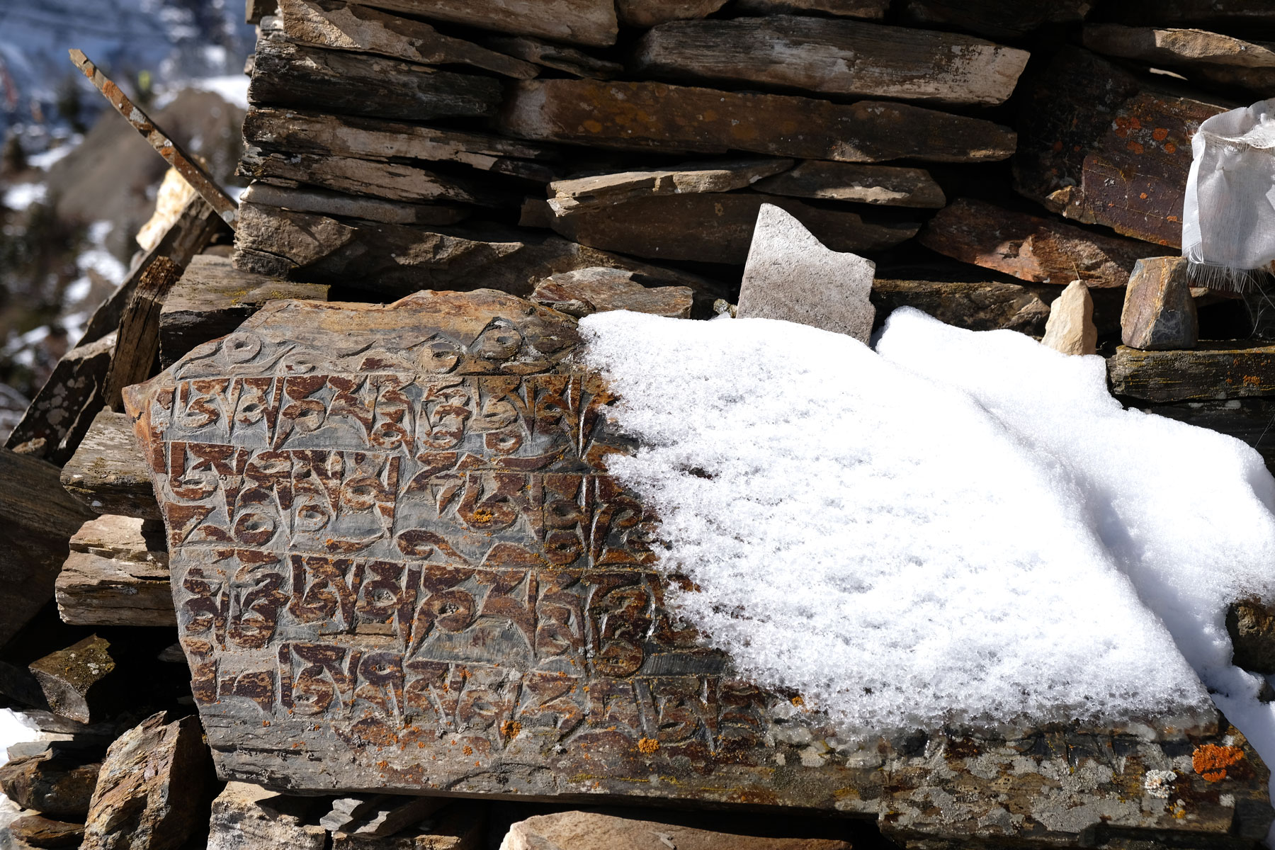 Tibetische Schriftzeichen auf einer schneebedeckten Steintafel.