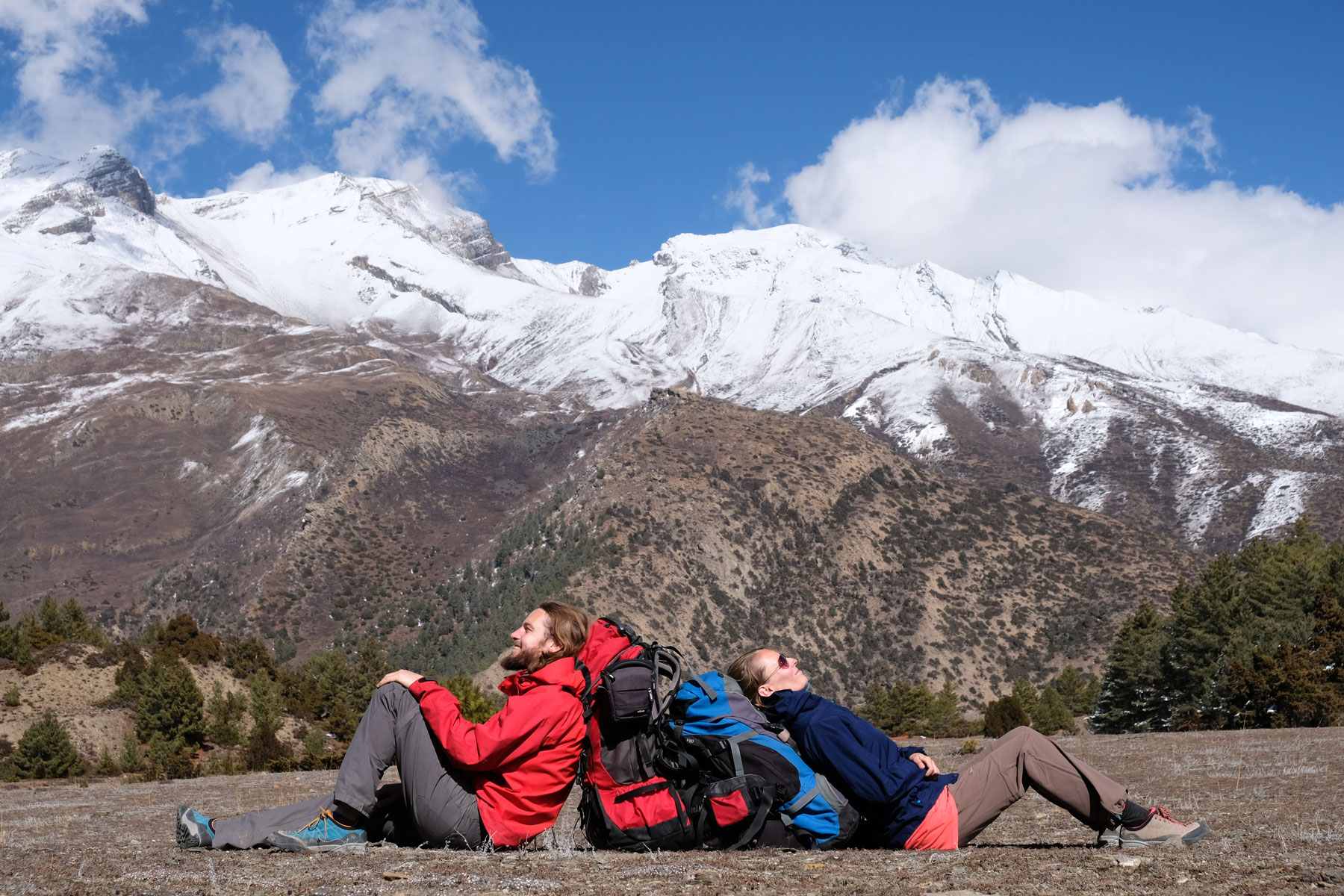 Sebastian und Leo sitzen an ihre Rucksäcke gelehnt vor Bergen im Annapurnagebirge.