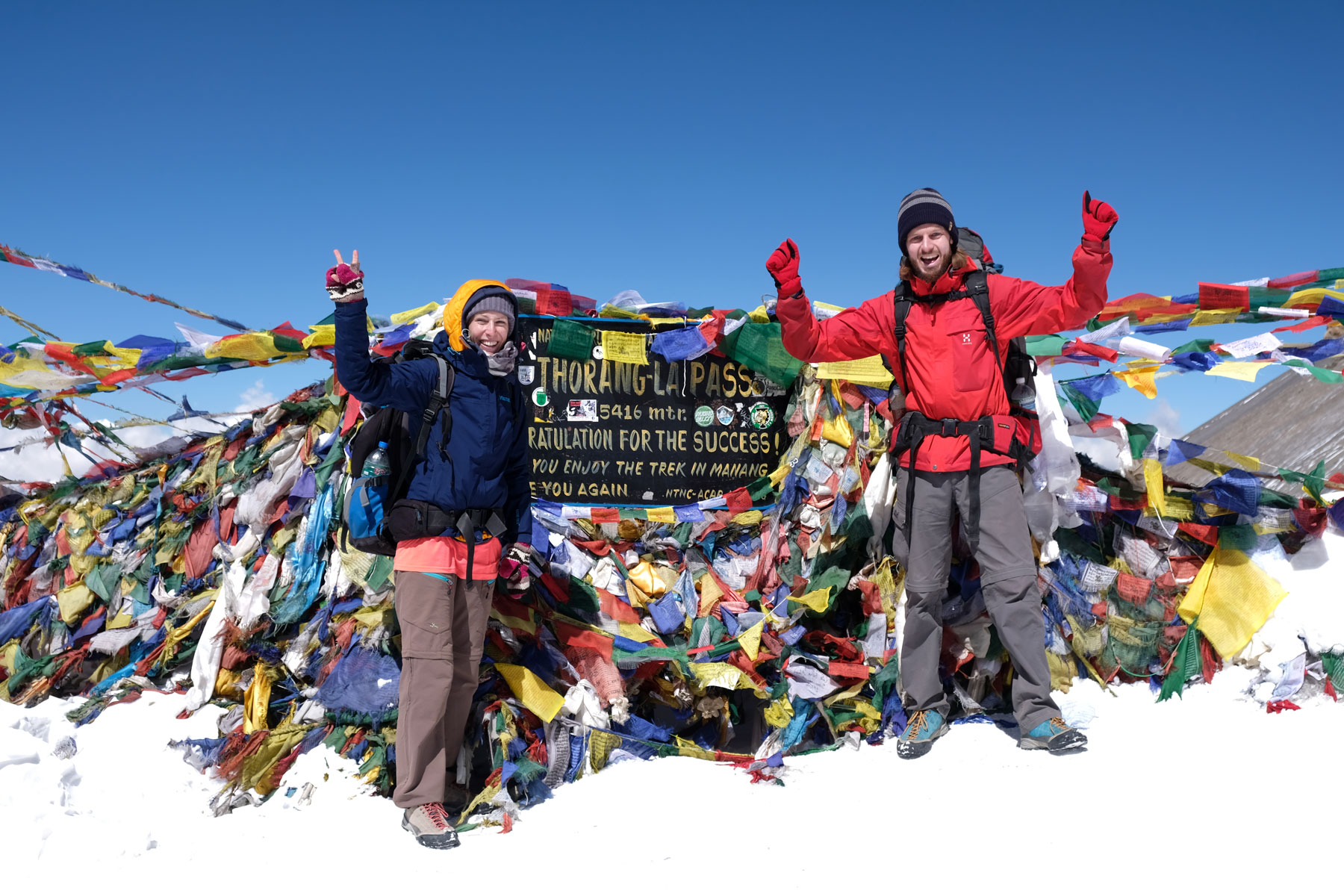 Leo und Sebastian jubeln vor Gebetsfahnen auf dem Thorong La Pass.