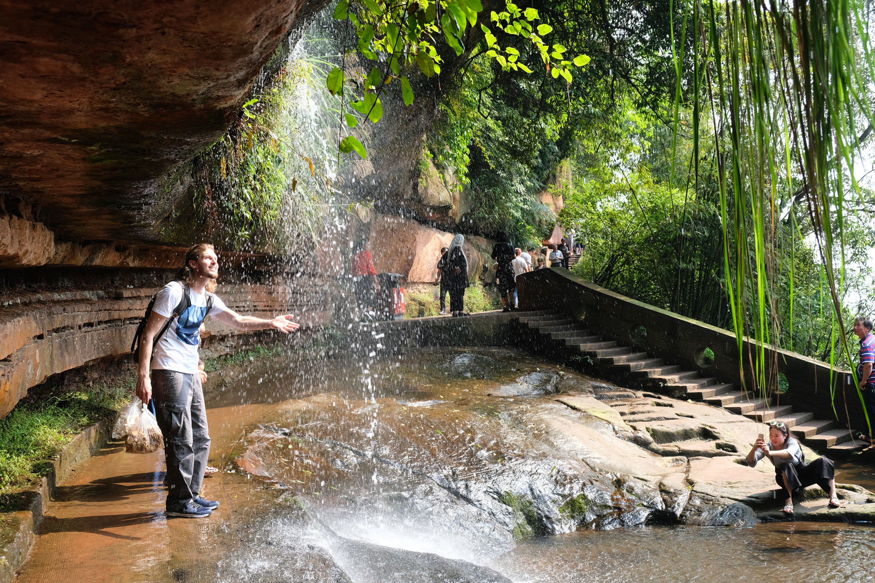 Sebastian hält seine Hand in einen kleinen Wasserfall im Shunan Zhuhai Nationalpark.