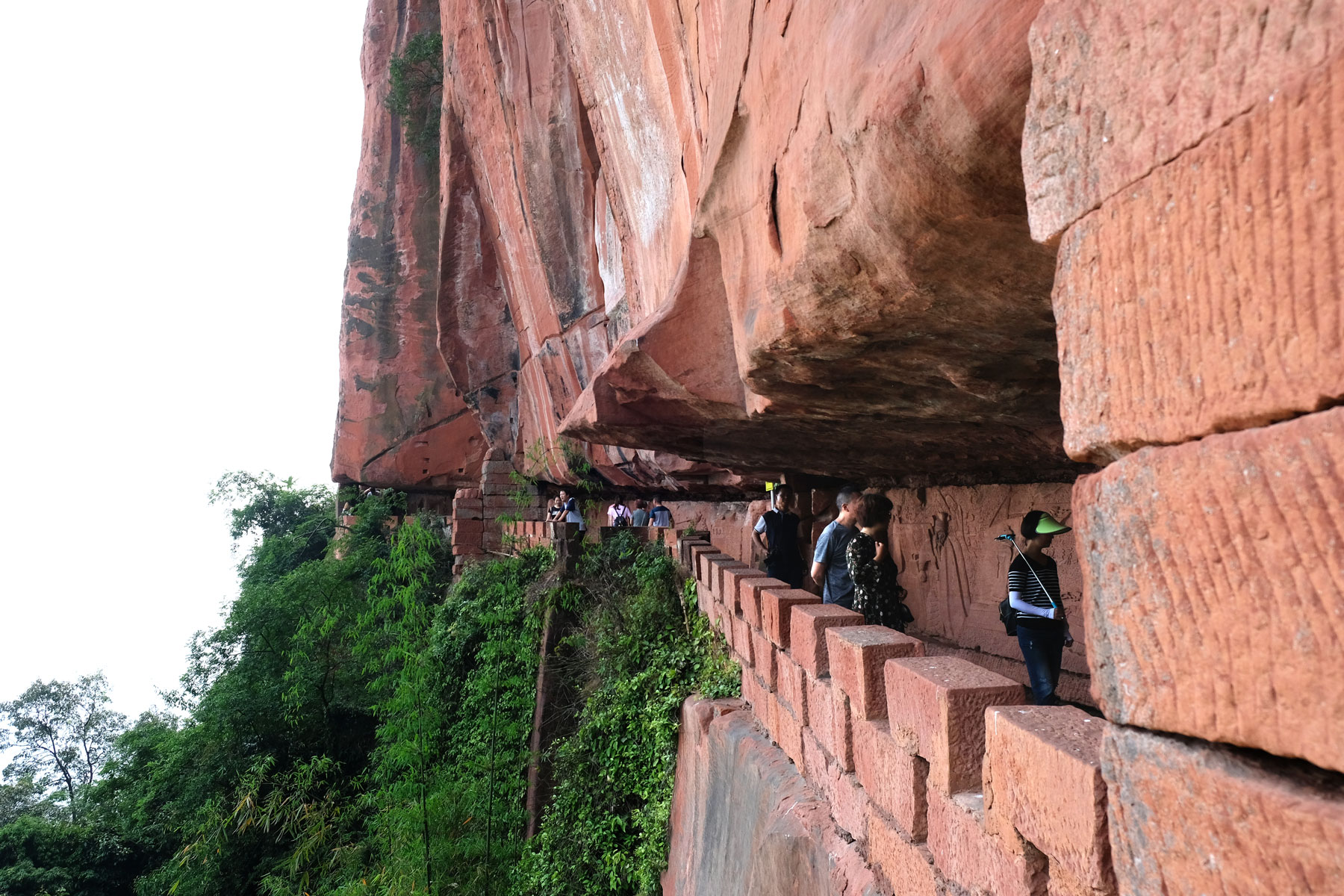 Chinesische Touristen gehen auf einem Weg, der in roten Fels gehauen wurde.