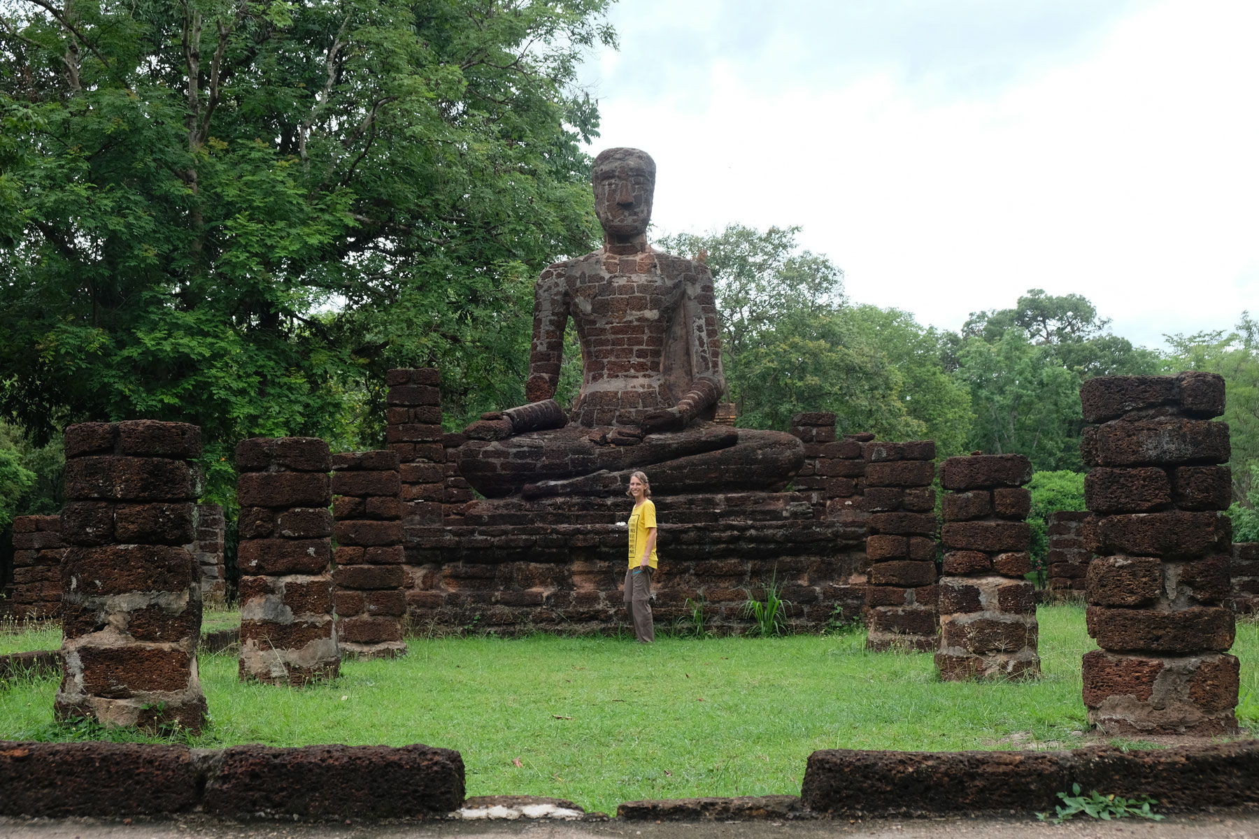 Leo steht in Kamphaeng Phet vor einer großen sitzenden Buddhastatue aus Stein.