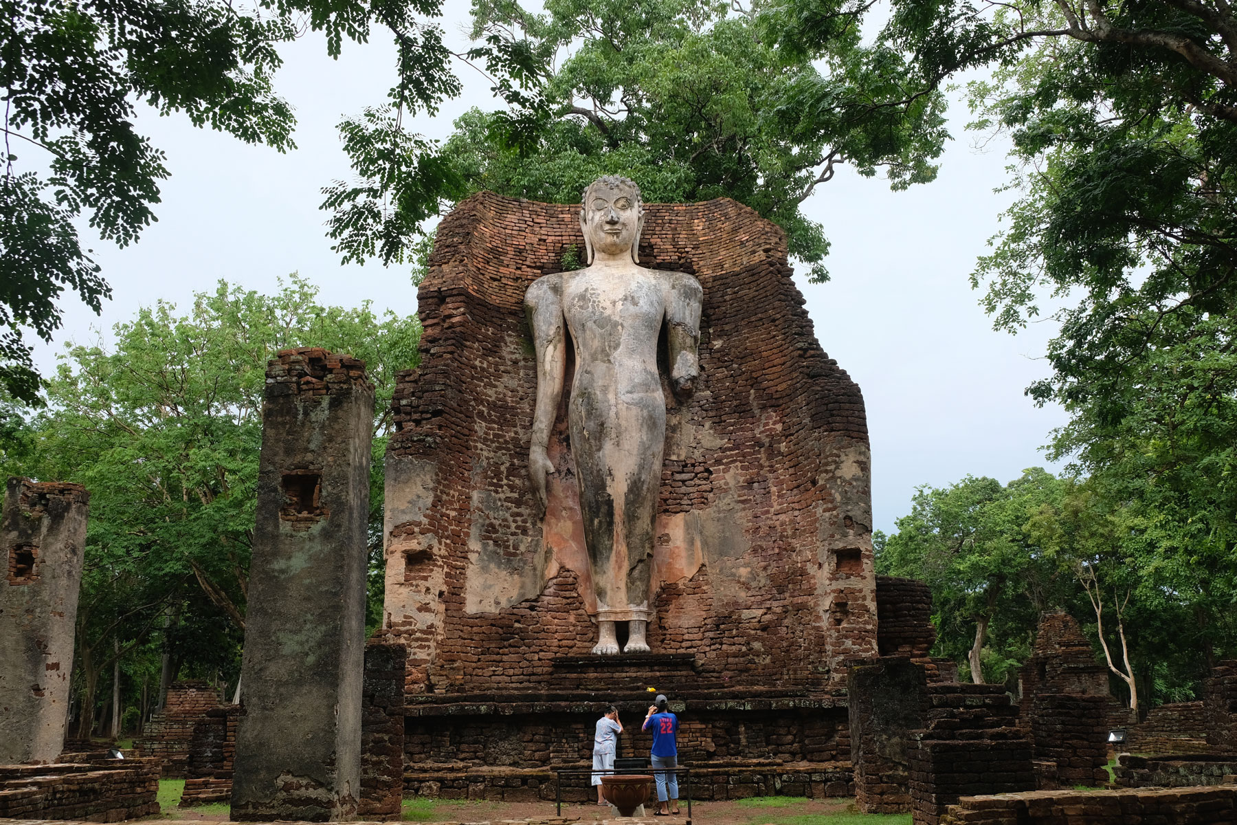 Zwei Menschen beten in Kamphaeng Phet vor einer etwa 15 Meter hohen steinernen Buddhastatue.