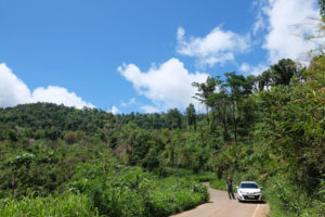 Sebastian steht neben einem weißen Auto in einem thailändischen Nationalpark.