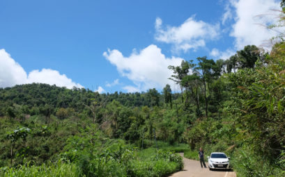 Sebastian steht neben einem weißen Auto in einem thailändischen Nationalpark.