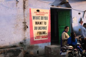 Indische Frauen vor einem Plakat, das die Frage aufwirft, was man vor dem eigenen Tod noch machen möchte.