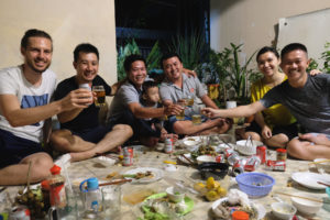 Sebastian sitzt mit Couchsurfing-Gastgeber Hanh und dessen Freunden auf dem Boden und stößt zu Ehren von Hanhs Geburtstag mit ihnen an.