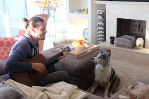 Sebastian spielt Hund Ellie ein Lied auf der Gitarre vor. Sie hört gespannt zu.