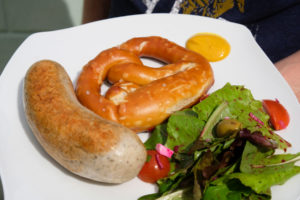 Bratwurst, Brezel und Salat liegen auf einem Teller.