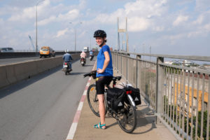 Leo steht mit ihrem Fahrrad auf der großen Brücke über den Mekong bei HCMC in Vietnam.
