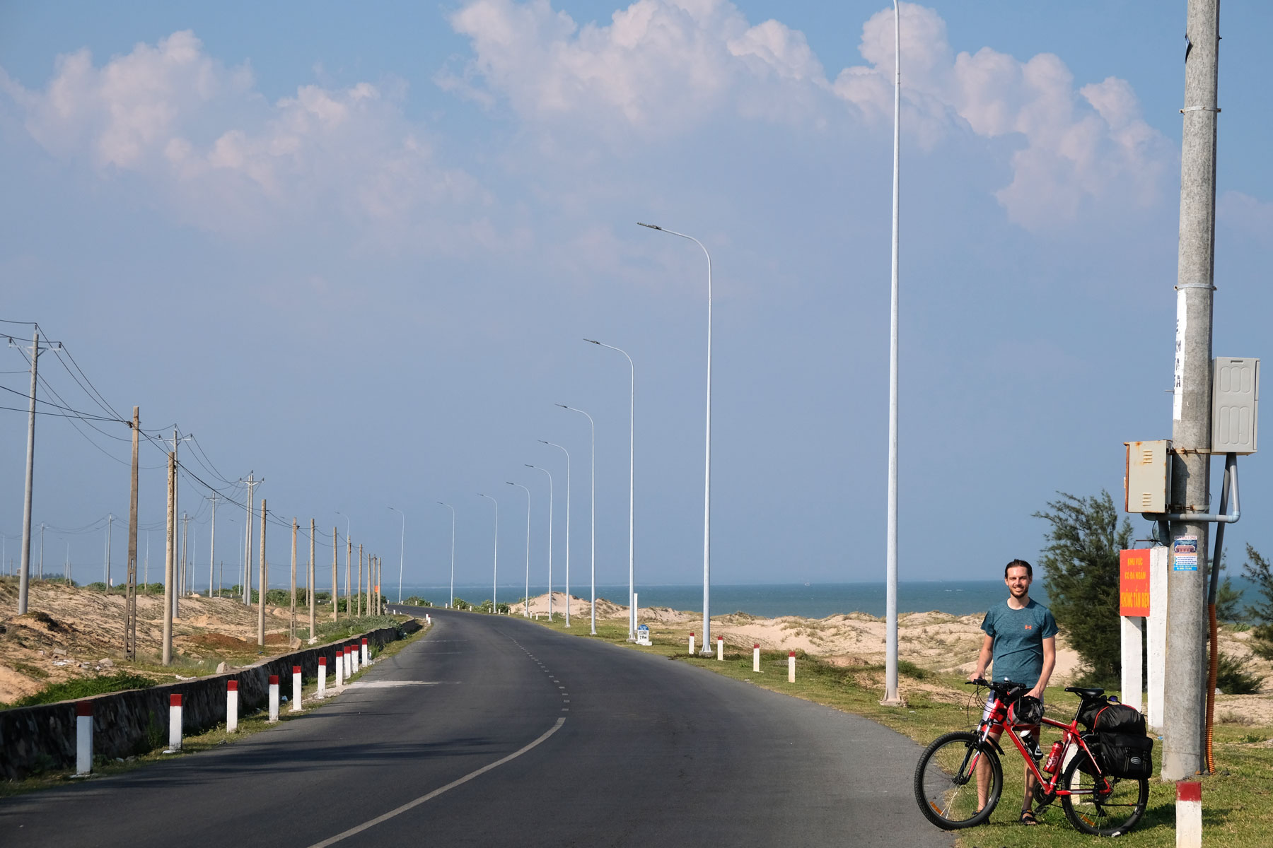 Sebastian steht mit seinem Fahrrad an der ruhigen Küstestraße im Süden Vietnams.