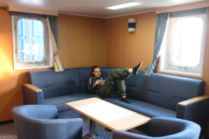 Sebastian liegt im Aufenthaltsraum für Passagiere auf einem Sofa.