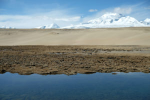 Ein kleiner See wird von Sanddünen abgelöst, die ihrerseits in Eisberge übergehen.