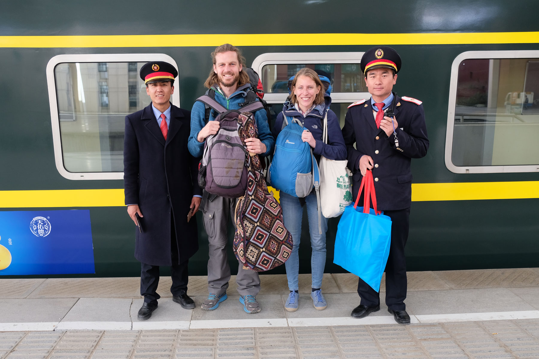 Leo und Sebastian stehen mit zwei Bahnhofsmitarbeitern vor ihrem Zug in Lhasa in Tibet.