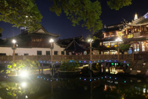 In der bei Nacht beleuchteten Altstadt von Shanghai spiegeln sich die Häuser im Wasser.