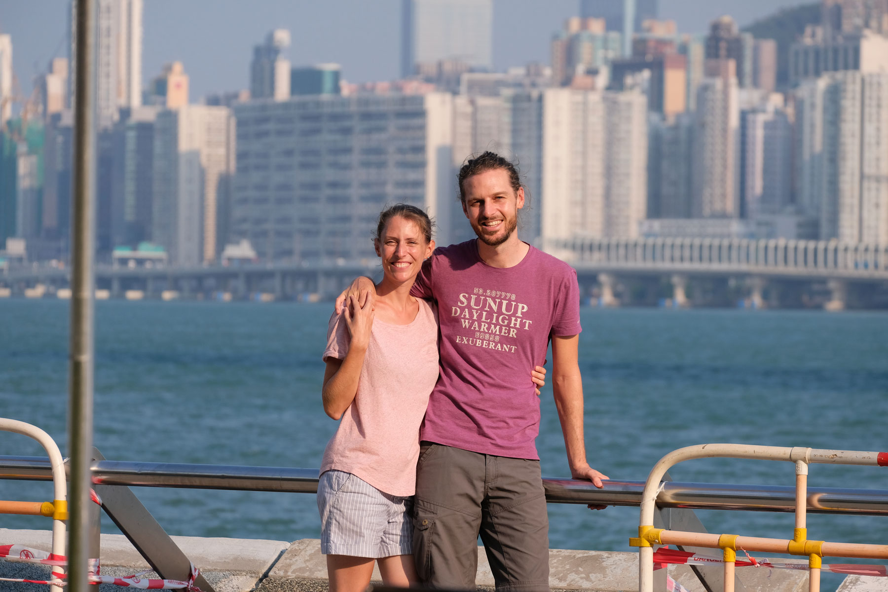 Leo und Sebastian von eins2frei stehen an der Promenade vor der Skyline der Hongkong Island.