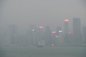 Ein Schiff mit roten Segeln fährt vor der Skyline Hongkongs vorbei, die im Nebel versinkt.