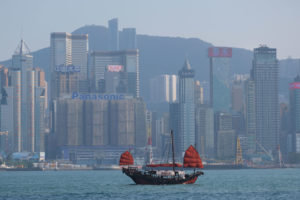 Ein Schiff mit roten Segeln fährt vor der Skyline Hongkongs vorbei