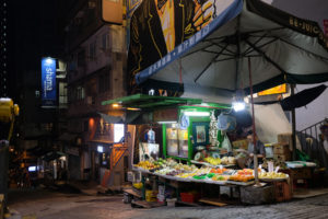 Ein beleuchteter Stand auf der Straße verkauft in der Dunkelheit Obst und Gemüse in Hongkong.