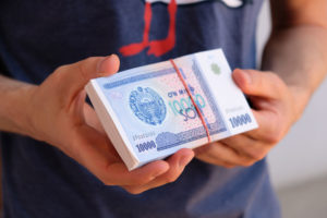 Ein Bündel usbekischer Som Geldscheine in zwei Händen.