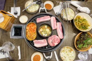 Ein Tisch ist für das koreanische Barbeque vorbereitet, bei dem dicke Scheiben Fleisch gegrillt werden.