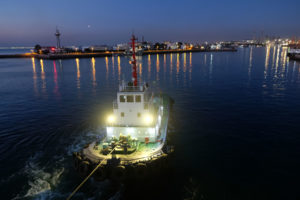 Ein Schleppschiff zieht in der Dunkelheit unsere Fähre aus dem Hafen Qingdao in China.