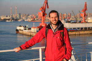 Sebastian steht an der Rehling unserer Fähre nach Südkorea, hinter ihm der Hafen von Qingdao in China.