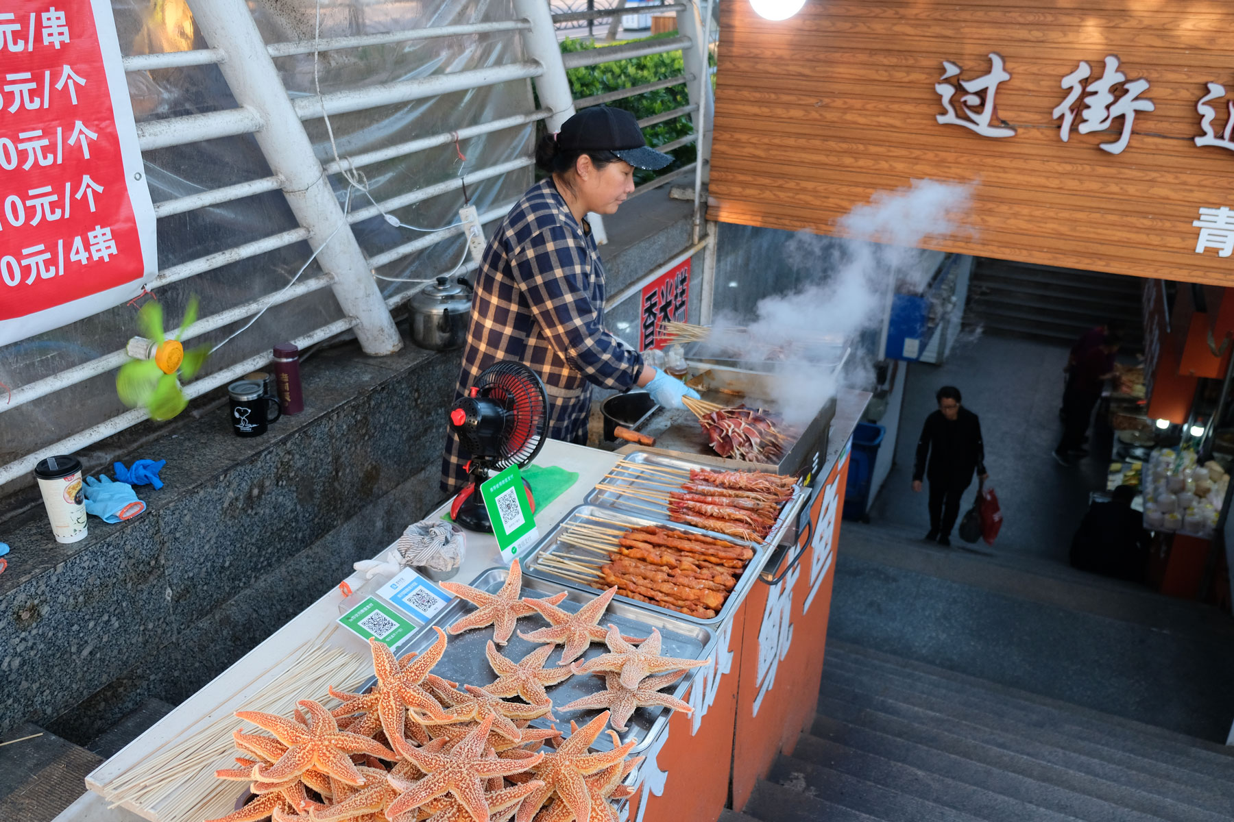 Eine Frau verkauft Seesterne und Fleischspieße in Qingdao in China.