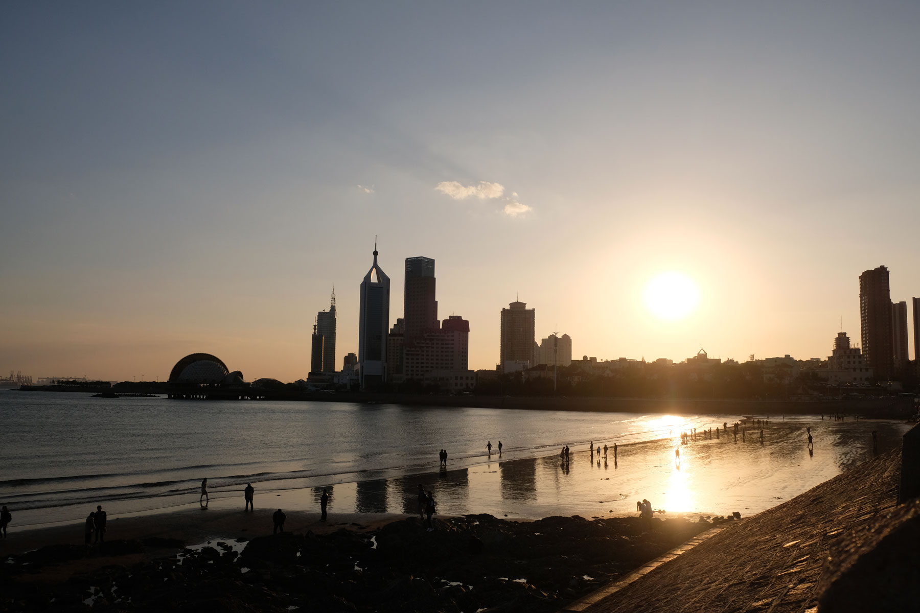 Die Sonne geht hinter den Hochhäusern von Qingdao unter.