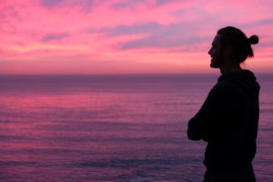 Sebastian steht vor einem lila verfärbten Abendhimmel am Meer.