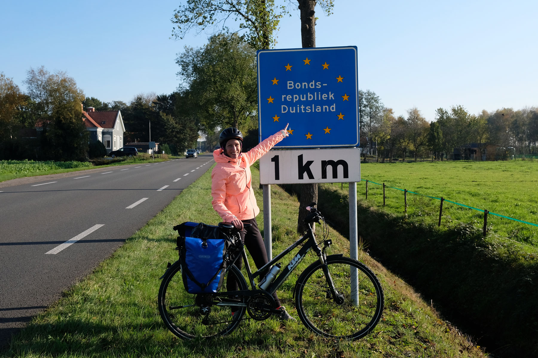 Leo steht mit ihrem Fahrrad vor einem Schild "Bundesrepublik Deutschland - 1 km".