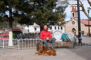 Sebastian und ein Straßenhund sitzen auf der Plaza von Creel in Mexiko.